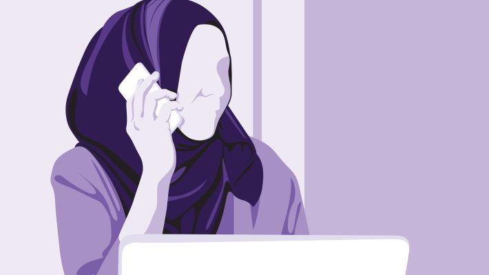 A woman in a headscarf speaking on the phone whilst looking at a laptop