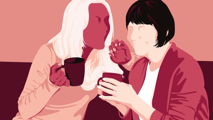 Two women sitting on the sofa chatting enthusiastically over a hot beverage